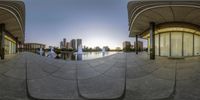 a fish eye lens view of a fountain and buildings with a person walking in the distance