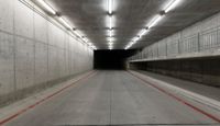 a tunnel with the floor almost covered by concrete slabs and red striped pavement below a large cement structure