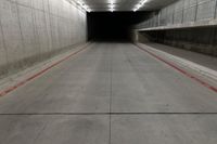 a tunnel with the floor almost covered by concrete slabs and red striped pavement below a large cement structure