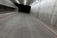 a tunnel with the floor almost covered by concrete slabs and red striped pavement below a large cement structure