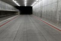 a tunnel with the floor almost covered by concrete slabs and red striped pavement below a large cement structure