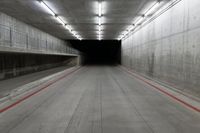 a tunnel with the floor almost covered by concrete slabs and red striped pavement below a large cement structure