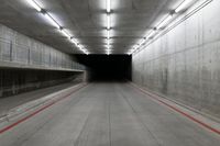 a tunnel with the floor almost covered by concrete slabs and red striped pavement below a large cement structure