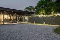 gravel driveway with car parking at dusk and modern house lighting on one wall and trees