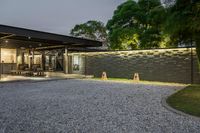 gravel driveway with car parking at dusk and modern house lighting on one wall and trees