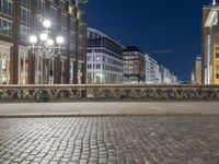 a city street at night with an empty sidewalk and lights shining on the building along the street