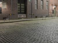an empty sidewalk of bricks with a round shaped sidewalk medallion on it at night, with the door in