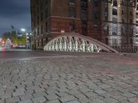 the sidewalk is brick with a bridge on top it in the city at night,