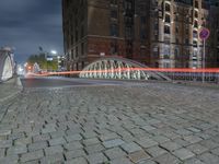 the sidewalk is brick with a bridge on top it in the city at night,