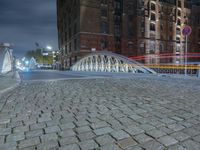 the sidewalk is brick with a bridge on top it in the city at night,