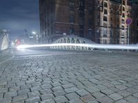 the sidewalk is brick with a bridge on top it in the city at night,