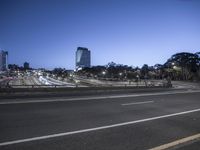 a highway is seen at night near a tall tower with skyscrapers in the distance