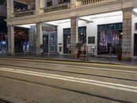 the light rail at night on the street is illuminated by some lights in front of the building