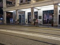 the light rail at night on the street is illuminated by some lights in front of the building