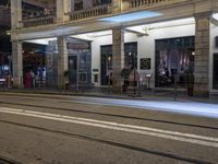 the light rail at night on the street is illuminated by some lights in front of the building