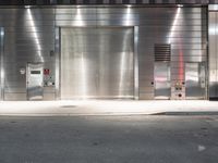 an empty street with a metallic door at night with white lines in the road on both sides