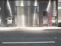 an empty street with a metallic door at night with white lines in the road on both sides