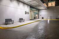 empty benches lined up outside a building at night time on a rainy day with the sidewalk painted yellow