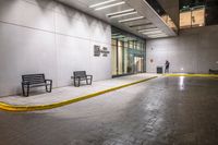 empty benches lined up outside a building at night time on a rainy day with the sidewalk painted yellow