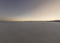 a person on some snow skate boards in the desert at sunset, while other people are walking down the road