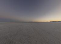 a person on some snow skate boards in the desert at sunset, while other people are walking down the road