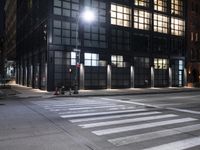 an intersection that has a crosswalk at night in a city at night time with street lights on and buildings near by