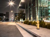 fire hydrant in front of a building near streetlights at nighttime, with the building behind the yellow fire hydrant