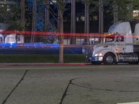 an image of a semi truck on the road at night with lights passing through the street