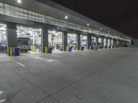 a parking garage with several doors and trash cans around it at night time as traffic passes by