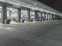 a parking garage with several doors and trash cans around it at night time as traffic passes by