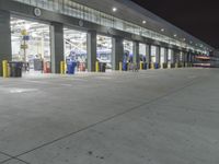 a parking garage with several doors and trash cans around it at night time as traffic passes by