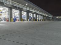 a parking garage with several doors and trash cans around it at night time as traffic passes by