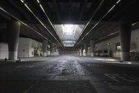 an empty street under a bridge in the dark of night time, with light streaming out from between some columns