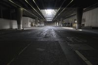 an empty street under a bridge in the dark of night time, with light streaming out from between some columns