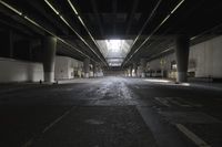 an empty street under a bridge in the dark of night time, with light streaming out from between some columns