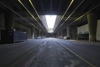 an empty street under a bridge in the dark of night time, with light streaming out from between some columns