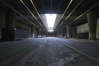 an empty street under a bridge in the dark of night time, with light streaming out from between some columns