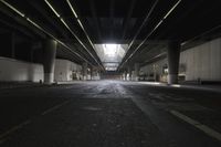 an empty street under a bridge in the dark of night time, with light streaming out from between some columns