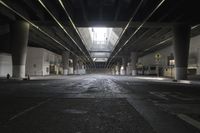 an empty street under a bridge in the dark of night time, with light streaming out from between some columns