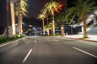 an empty street is in a blurry photograph with palm trees on either side and building to the right