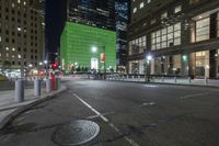 there is a bright green building behind the city buildings at night - - - in this particular area of the street