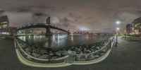 the view looking out towards a bridge over water at night time, surrounded by rocks and large buildings