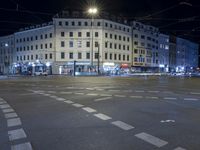 a city street with an intersection and a large white building at night time under a street light
