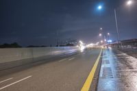 a long highway with light street lights at night in front of the city wall and overpass