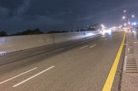 a long highway with light street lights at night in front of the city wall and overpass