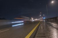 a long highway with light street lights at night in front of the city wall and overpass