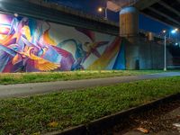 a mural in a tunnel by the highway at night with trees around it and two people near by