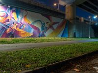 a mural in a tunnel by the highway at night with trees around it and two people near by