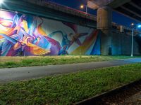 a mural in a tunnel by the highway at night with trees around it and two people near by