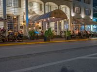 an outdoor restaurant on the side of the road in front of a white building at night